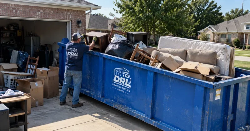 Household junk including furniture, mattresses, boxes, and bags filling a roll-off dumpster during a home cleanout