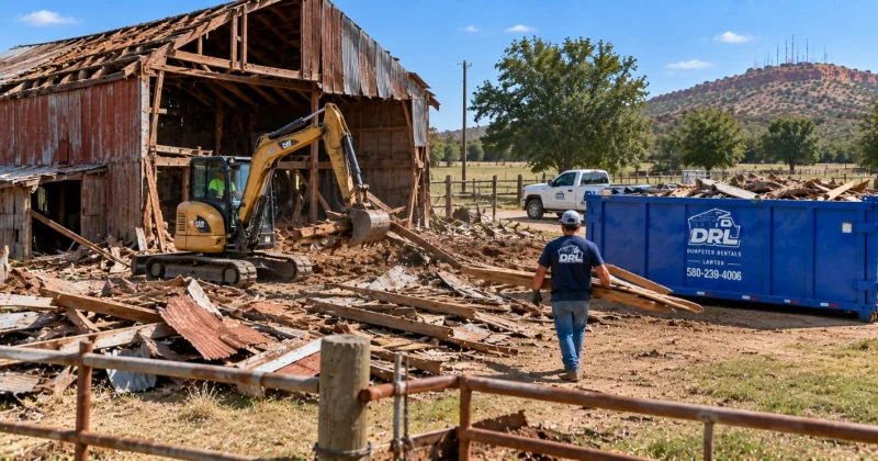 Barn demolition debris including lumber, corrugated metal, roofing materials, and structural wood being cleared into a dumpster near Lawton, Oklahoma
