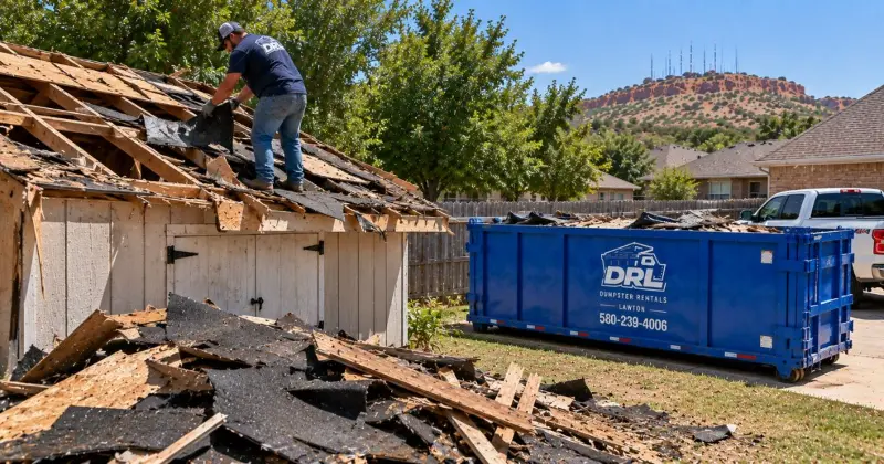 Shed roof demolition debris including shingles, plywood, and wood framing being loaded into a dumpster in Lawton, Oklahoma